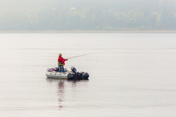 men Fisherman catches fish standing on an inflatable boat in the Volga River against the backdrop of the Zhiguli Mountains on a warm summer day