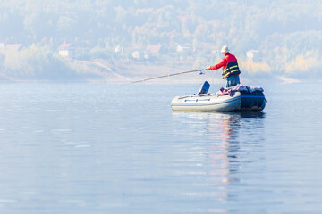 men Fisherman catches fish standing on an inflatable boat in the Volga River against the backdrop of the Zhiguli Mountains on a warm summer day