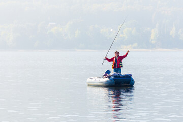 men Fisherman catches fish standing on an inflatable boat in the Volga River against the backdrop of the Zhiguli Mountains on a warm summer day
