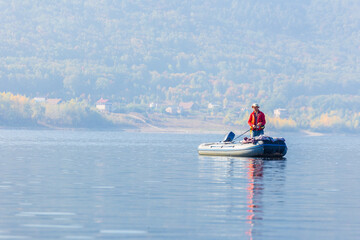 men Fisherman catches fish standing on an inflatable boat in the Volga River against the backdrop of the Zhiguli Mountains on a warm summer day