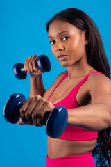 Young black woman lifting weights on blue background