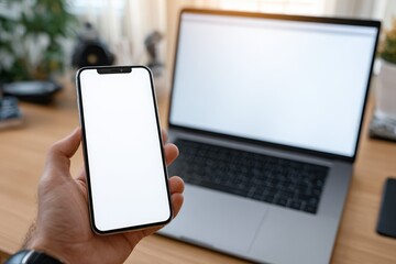 Hand holding phone with blank screen, beside laptop