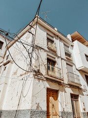 Old derelict building with electricity wires and weathered stucco walls under a blue sky. Andalucia, Spain.