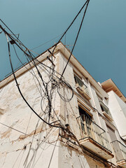 Old derelict building with electricity wires and weathered stucco walls under a blue sky. Andalucia, Spain.