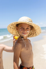 Father, applying sun cream on his  cute blond boy, playing on the sea, hat, sunglasses, swimsuit,...