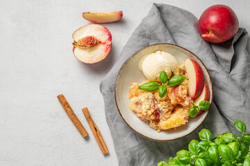 Peach crumble or cobbler with vanilla ice cream scoops and cinnamon on a plate on a light background
