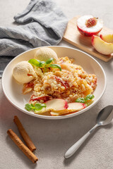 Peach crumble or cobbler with vanilla ice cream scoops and cinnamon on a plate on a light background