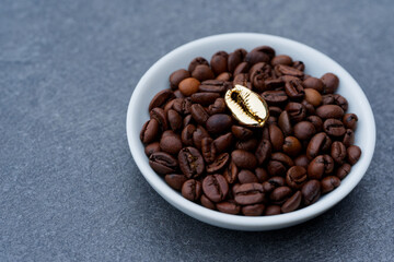 White plate with coffee beans and a golden decorative bean on dark table