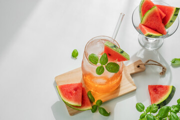 Watermelon mojito cocktail with ice and mint in a glass on a white background with fresh herb and sunlight.
