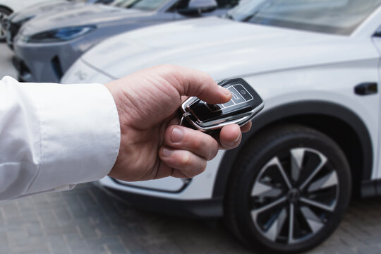 Fototapeta Businessman holding car keys near premium electric auto in store showroom parking lot. Car rental, car purchase and car showroom concept.