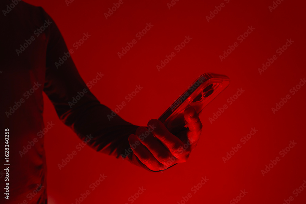Poster modern smartphone in a man's hand. the man holds the device under red studio light. the concept of s