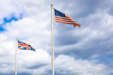 UK and US flags waving side by side on flagpoles against a cloudy sky, symbolizing international relations and historic ties