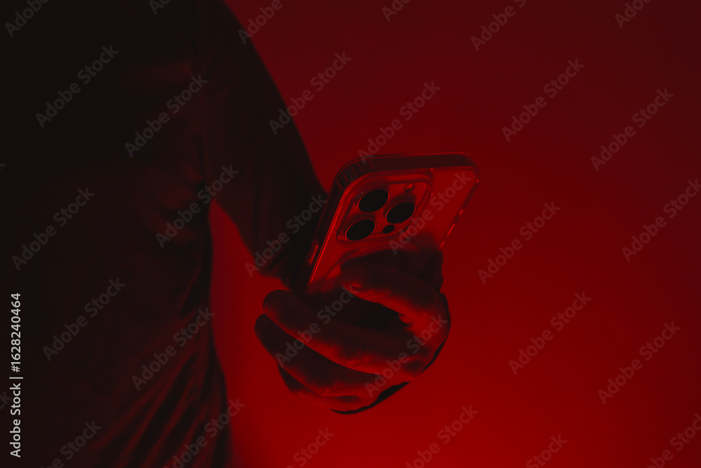 Poster modern smartphone in a man's hand. the man holds the device under red studio light. the concept of s
