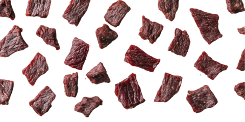 Dried beef jerky pieces scattered across a transparent background highlighting texture and rich color