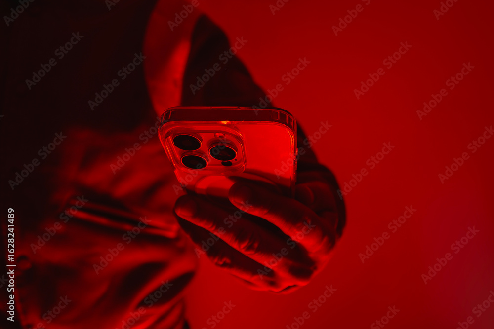 Poster modern smartphone in a man's hand. the man holds the device under red studio light. the concept of s