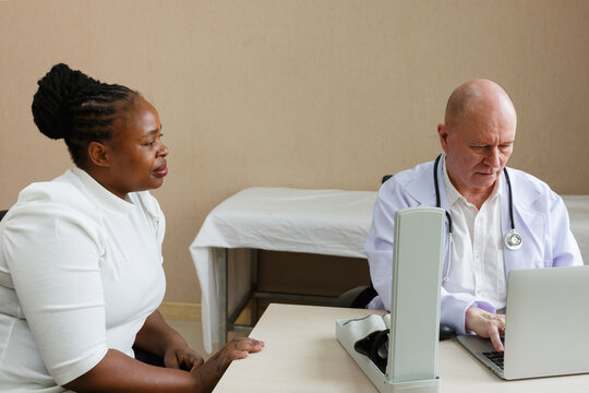 senior professional doctor using blood pressure monitor on african american female patient in a medical consultation clinic or examination room at hospital. healthcare, hospital service and insurance.