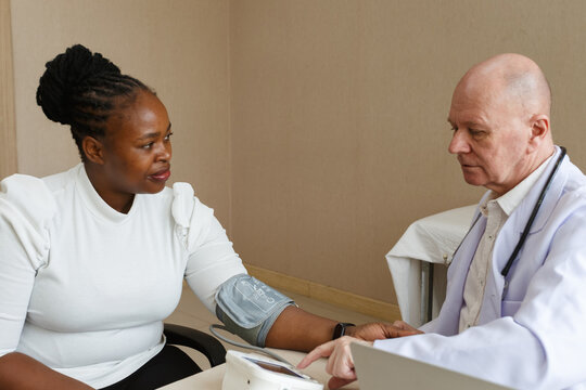 senior professional doctor using blood pressure monitor on african american female patient in a medical consultation clinic or examination room at hospital. healthcare, hospital service and insurance. - Powered by Adobe