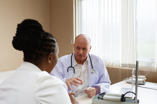 senior professional doctor using blood pressure monitor on african american female patient in a medical consultation clinic or examination room at hospital. healthcare, hospital service and insurance.