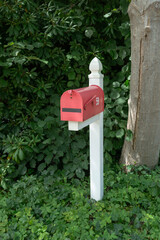 Red letterbox mounted on a white post surrounded by green bushes and trees