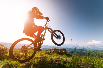 Young man riding through the air on a mountain bike on the back wheel. Fitness, extreme sports and mountain bike with man outdoors for cycling, jumping and adventure. Adrenaline junkie