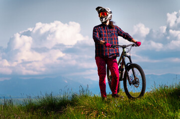 Portrait of a cyclist standing with his bicycle against a dramatic sky with cumulus clouds. Handsome young man biking in the countryside