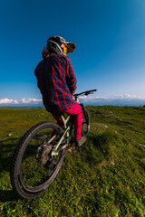 Back view wide angle of mountain bike and man in mountains against mountain range and hills with clouds and blue sky. Extreme sports concept, relaxation during training