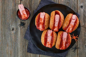 Halloween background. Homemade hot dogs with bloodied fingers on dark table for Halloween. Themed food for celebration party Halloween. Copy space.