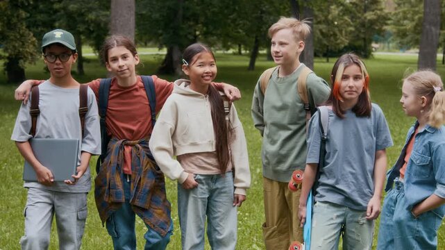 Group of cheerful diverse gen alpha children chatting with one another while spending time in park after school