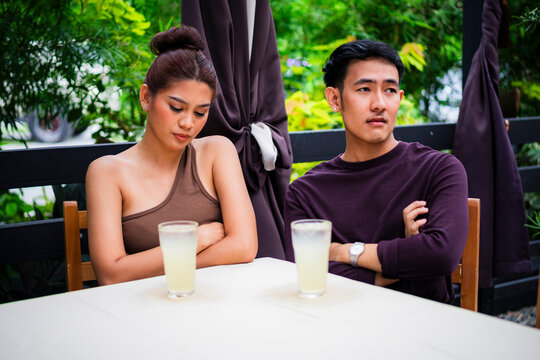 Frustrated young Asian couple avoid eye contact during a failed date at an alfresco cafe.