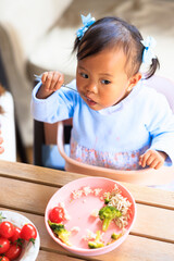 High view of Little girl sitting at the table eating independently with a spoon