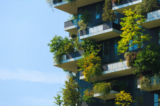 A unique building showcases balconies adorned with lush plants and green energy in an urban setting under a clear sky. - Powered by Adobe