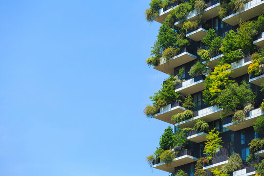 Vibrant vertical garden on energy efficient building, featuring lush greenery on balconies throughout the facade against a clear blue sky.