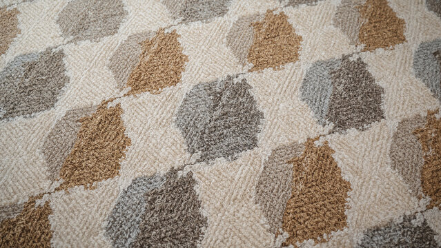 Close-up of a textured fabric with a repeating diamond pattern of leaves in beige brown and grey