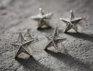 Four small, star-shaped, metallic accessories lie on a textured, light gray surface.  Details of the stars and their placement are emphasized