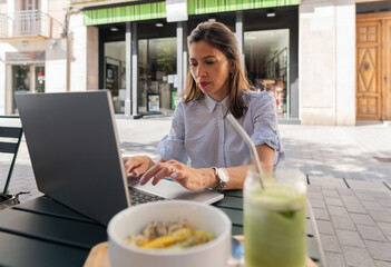 Businesswoman working on laptop while having breakfast at outdoor cafe