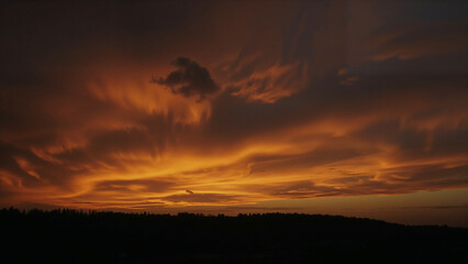 Obraz premium Dramatic Orange and Red Sunset Sky with Wispy Clouds Over Dark Horizon image photo