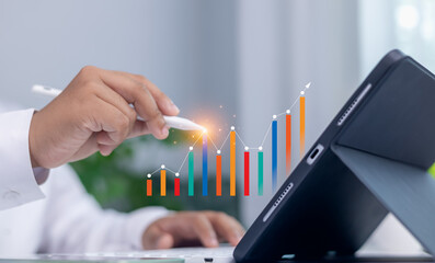 Financial growth, data analysis, strategic planning, and technology concept. Businessman hand using stylus on tablet with colorful digital bar graph and line chart overlay.
