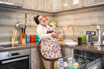 Woman talking on the phone while loading the dishwasher in the kitchen