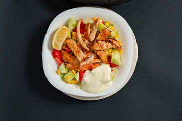 Caesar salad with chicken in a white plate. Dark background. Close up. Top view. Healthy food, keto diet, diet lunch concept.