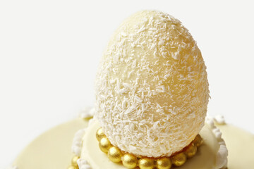 Delicious white chocolate easter egg resting on a cake decorated with gold and white chocolate
