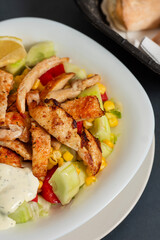 Caesar salad with chicken in a white plate. Dark background. Close up. Top view. Healthy food, keto diet, diet lunch concept.