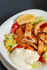 Caesar salad with chicken in a white plate. Dark background. Close up. Top view. Healthy food, keto diet, diet lunch concept.