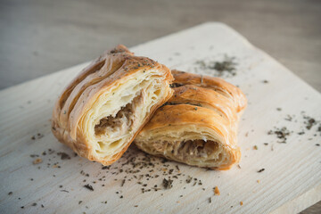 A close-up view of puff pastries sliced in half, showing their flaky layers and savory filling. Sprinkled aromatic herbs enhance the presentation, offering a rustic and appetizing scene.