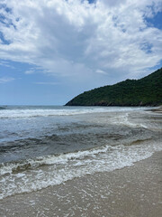 Beautiful beach with open sea and strong waves with a green mountain background, characterized by being a quiet place