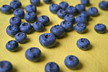 Close-up of blueberries scattered on yellow craft paper.