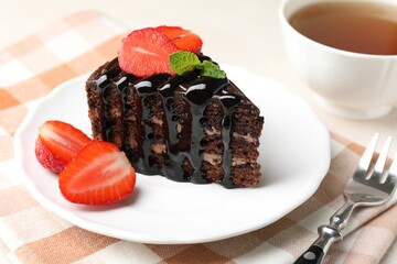 Piece of chocolate cake served with strawberries, tea and fork on table, closeup
