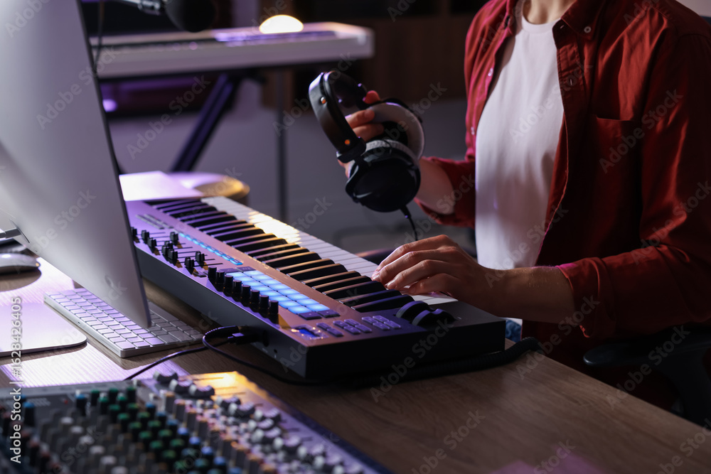 Poster man with headphones working with midi keyboard at table indoors, closeup