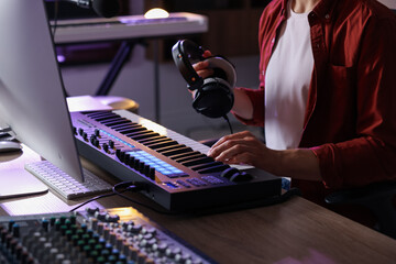 Man with headphones working with MIDI keyboard at table indoors, closeup