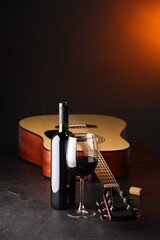 Acoustic guitar and red wine on black table with brown light, closeup. Space for text