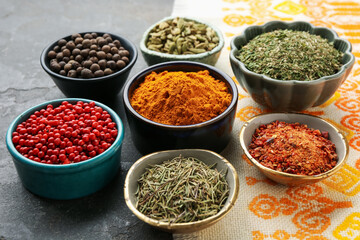 Many different aromatic spices in bowls on grey table with cloth, closeup